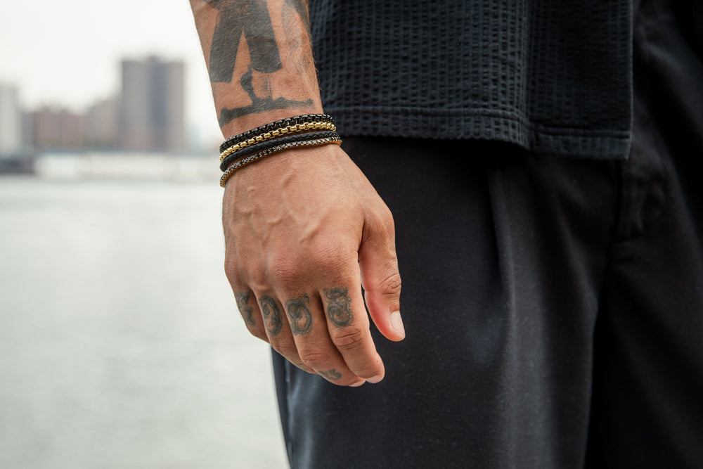 Side-by-side comparison of stainless steel and sterling silver men's jewelry bracelets on a stone surface