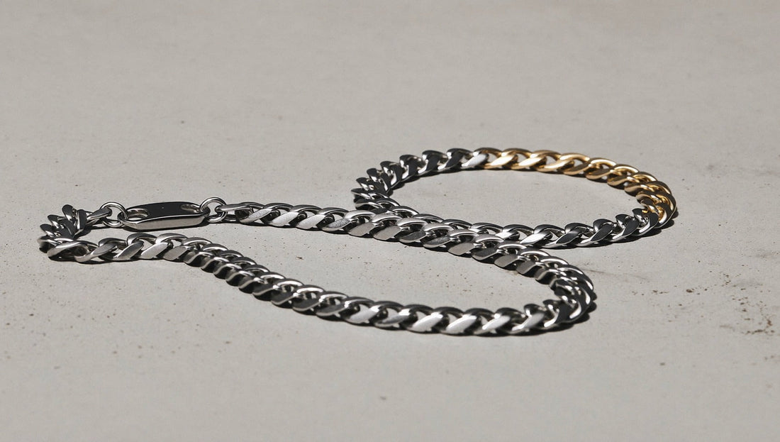 Stainless steel cuban link chains and a two-tone bracelet arranged on a minimal concrete surface with soft studio lighting
