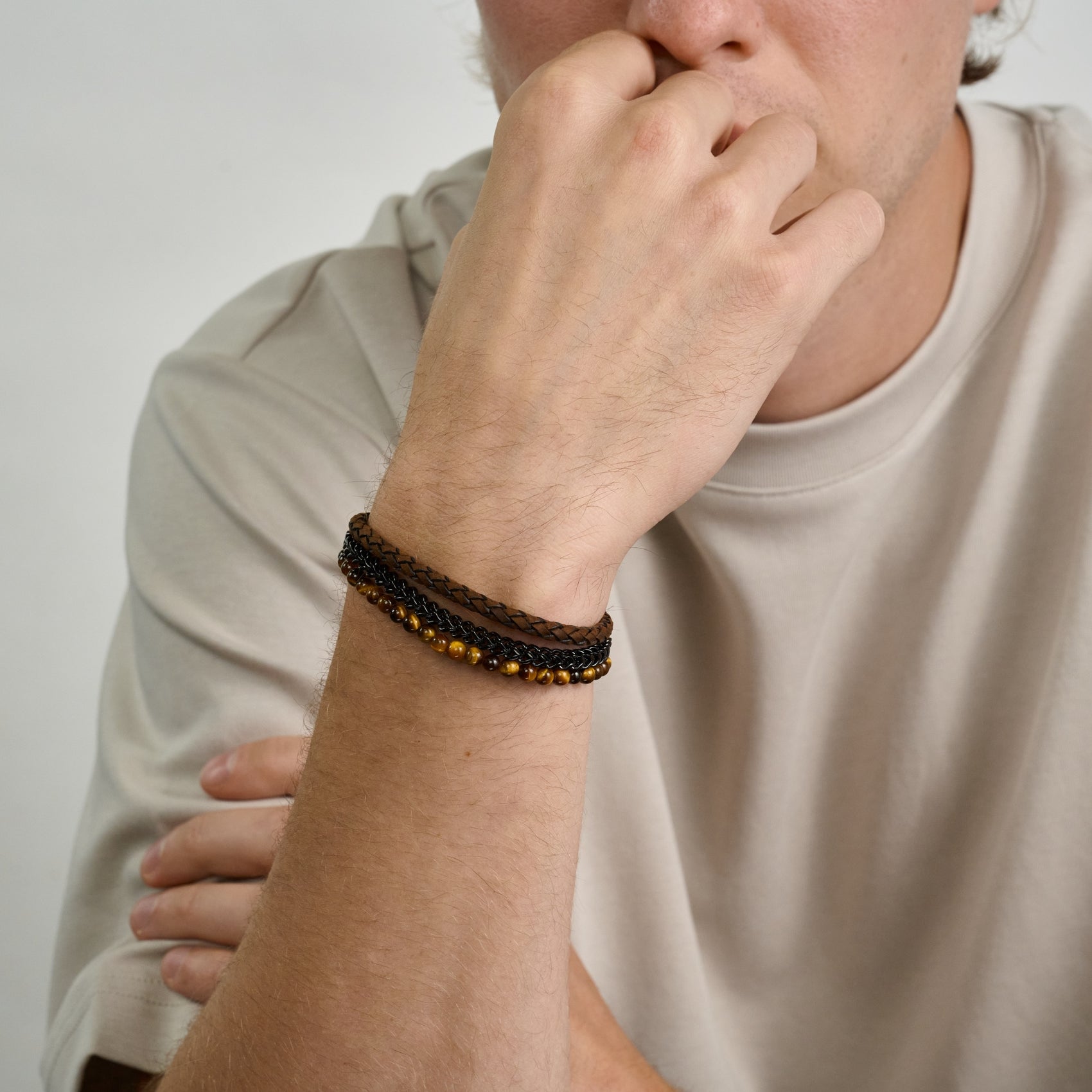 Men's bracelet stack with matte brown leather, polished black steel, and natural Tiger Eye stones  